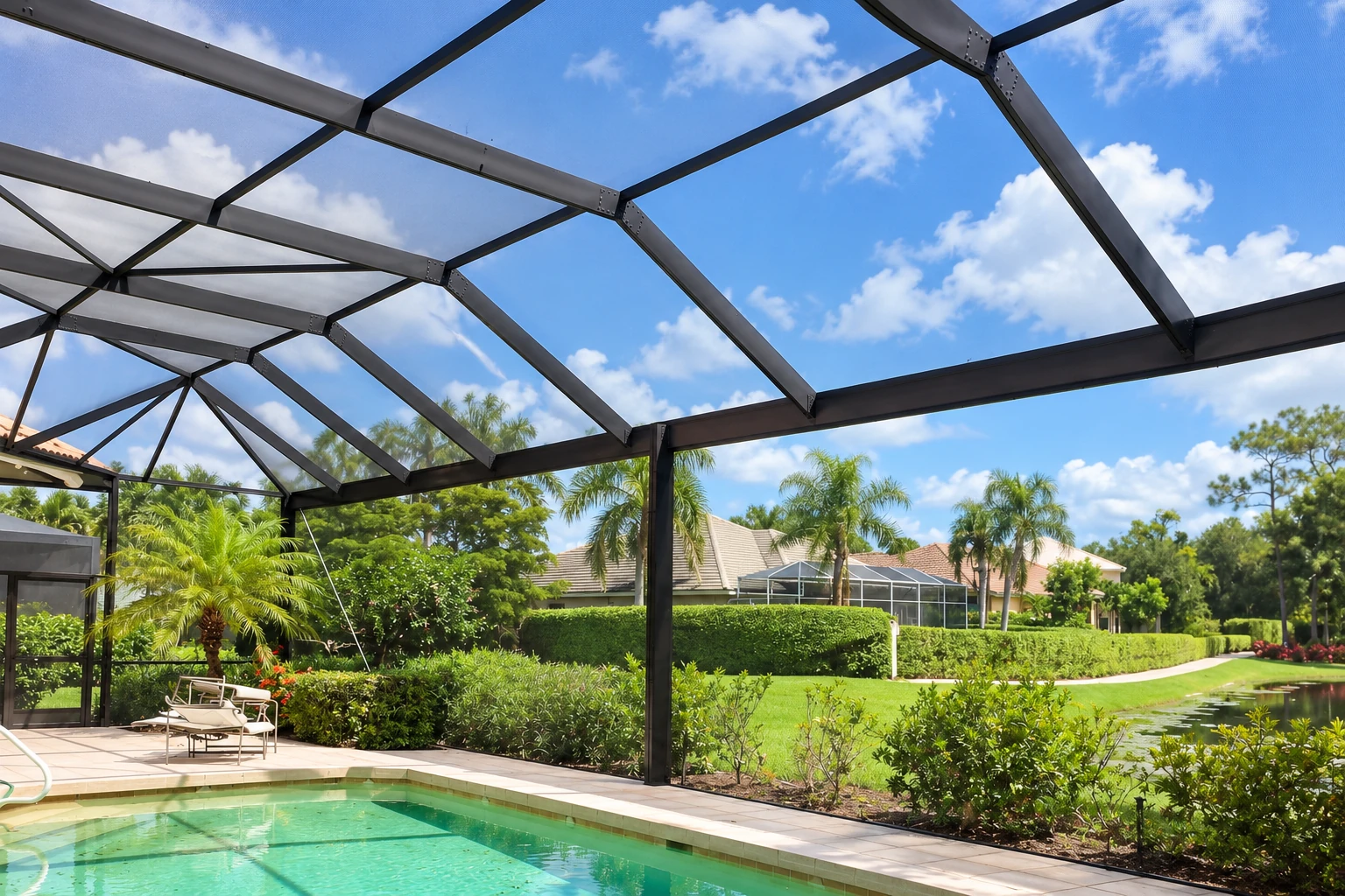 A black metal screen-room frame spans a backyard patio beside a swimming pool under a blue sky.