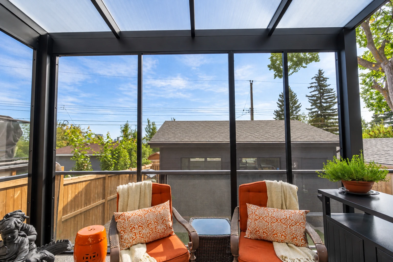 Screened patio room with a translucent roof, black framing, and orange cushioned chairs.